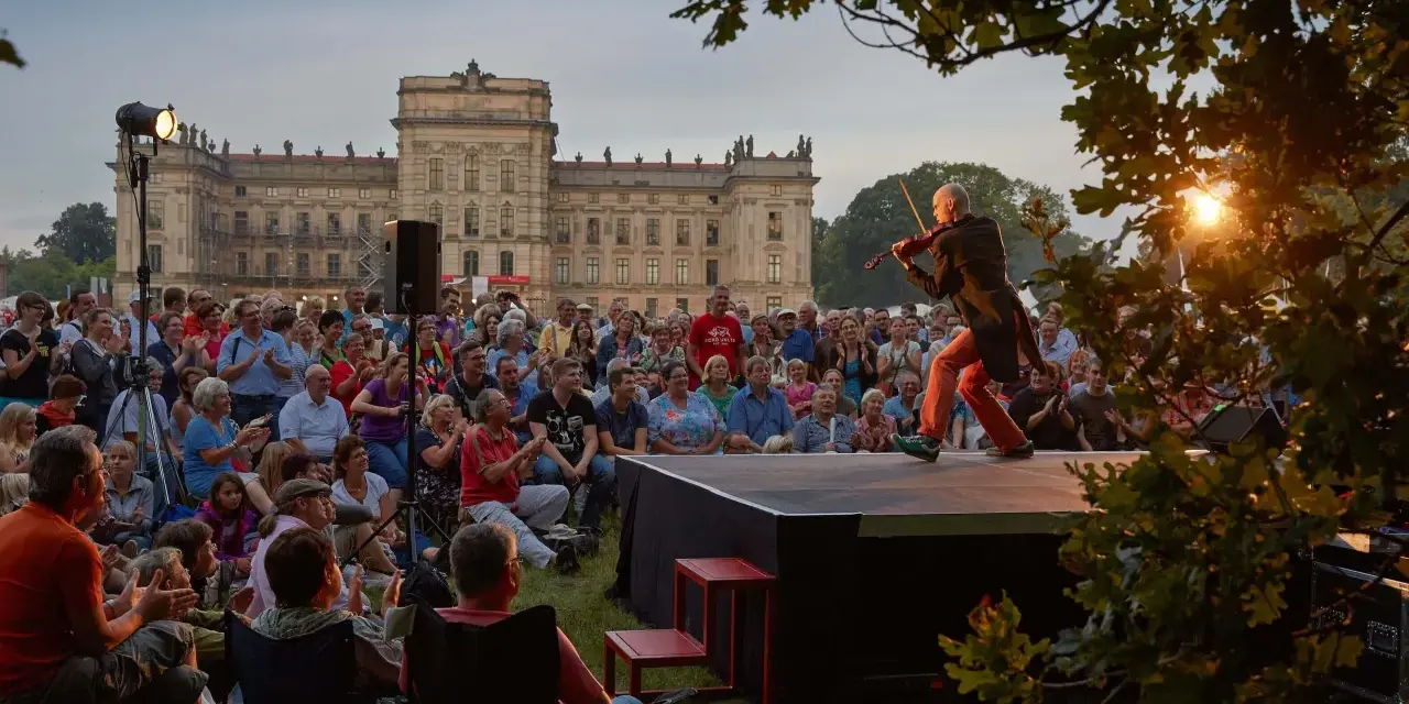 Ein Geiger spielt auf einer Bühne vor einem Schloss, während ein Publikum zusieht. Ein schönes Beispiel für Veranstaltungen an der Ostsee.