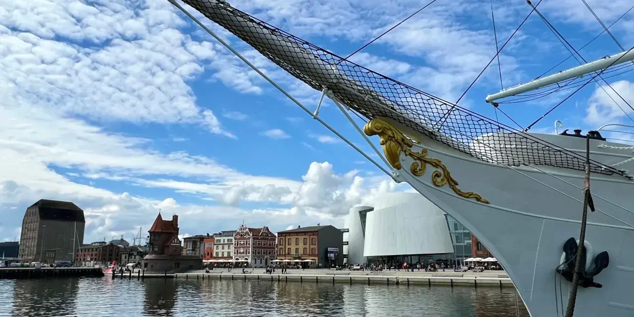 Die Gorch Fock in Stralsund, ein stolzes Segelschiff, liegt vor einer malerischen Kulisse mit historischen Gebäuden und moderner Architektur am Hafen.