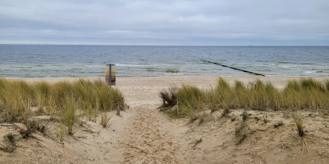 Pfad durch Dünen zum Strand Bansin. Das Meer ist ruhig, der Himmel bedeckt.