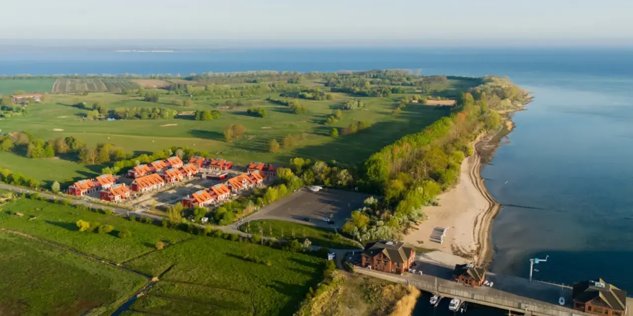Ferienhäuser am Meer, daneben ein Golfplatz. Ein kleiner Hafen mit Booten.