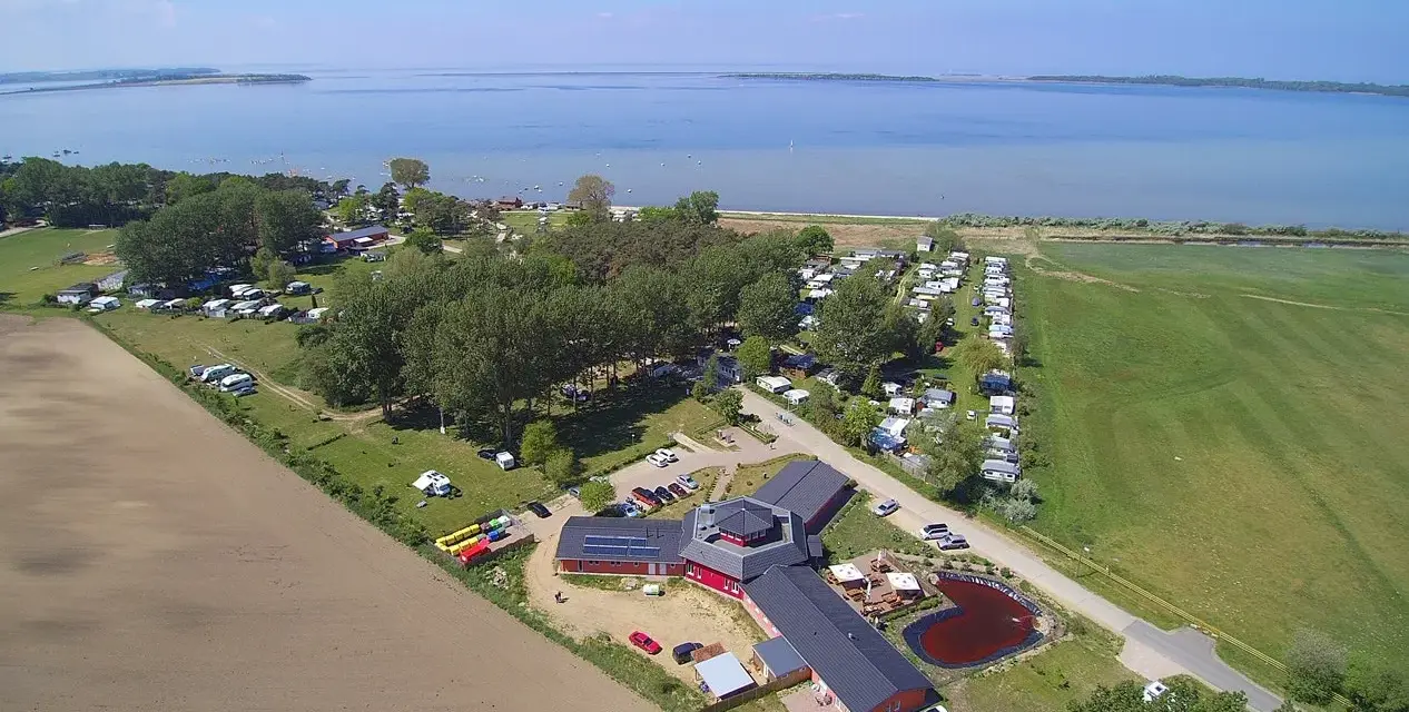 Luftaufnahme des pepelow campingplatzes mit Wohnmobilen, Bäumen und einem See im Hintergrund.