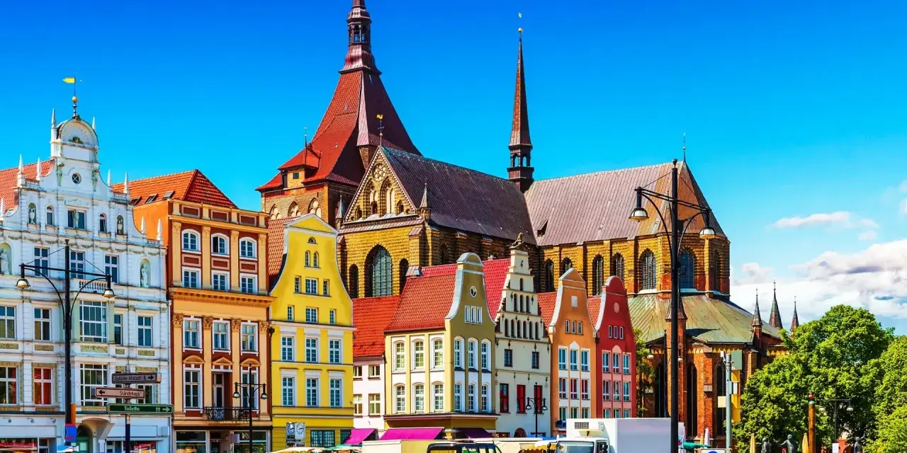 Bunte Giebelhäuser und die Marienkirche prägen das Bild der Rostocker Innenstadt. Ein sonniger Tag auf dem Platz.