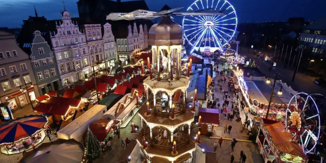 Ein beleuchteter Weihnachtsmarkt Mecklenburgische Seenplatte mit Riesenrad, Pyramide und Buden.