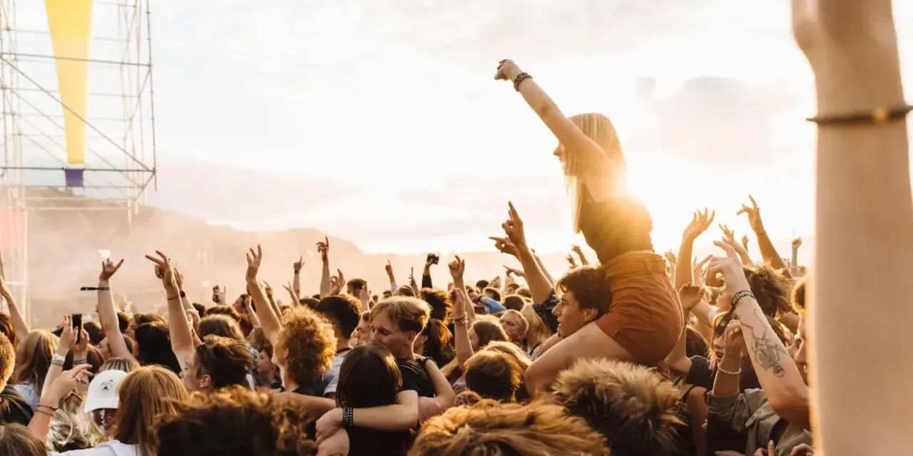 Menschen jubeln auf einem Festival in Rostock. Eine Frau sitzt auf den Schultern eines anderen Besuchers, während die Sonne untergeht.