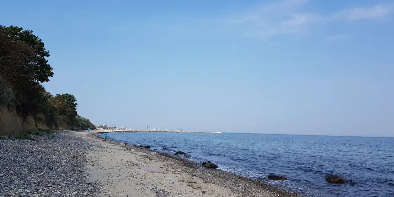 Ein ruhiger Tag am Wittenbeck Strand. Kies und Sand treffen auf das sanfte Meer, im Hintergrund eine Marina.