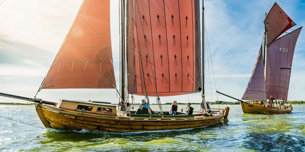 Zeesboot "Bill" segelt bei Ahrenshoop mit roten Segeln. Ein zweites Boot folgt.