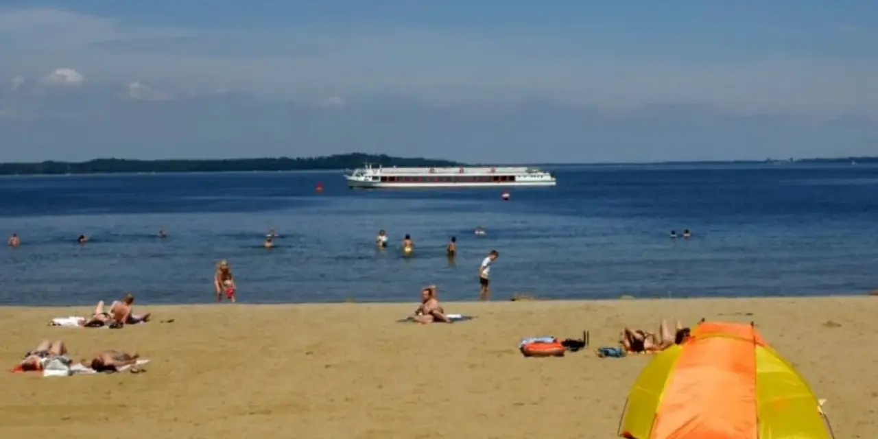 Sonne, Sand und ein Schiff auf dem Wasser – ein entspannter Tag am Schweriner Strand mit Badegästen und einer bunten Strandmuschel.