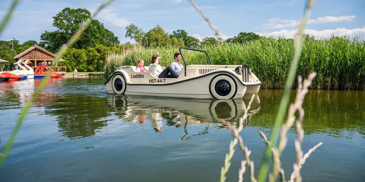 Familie genießt eine Fahrt mit einem Auto-Boot von Kiki's Bootsverleih auf einem ruhigen See, umgeben von üppigem Grün.