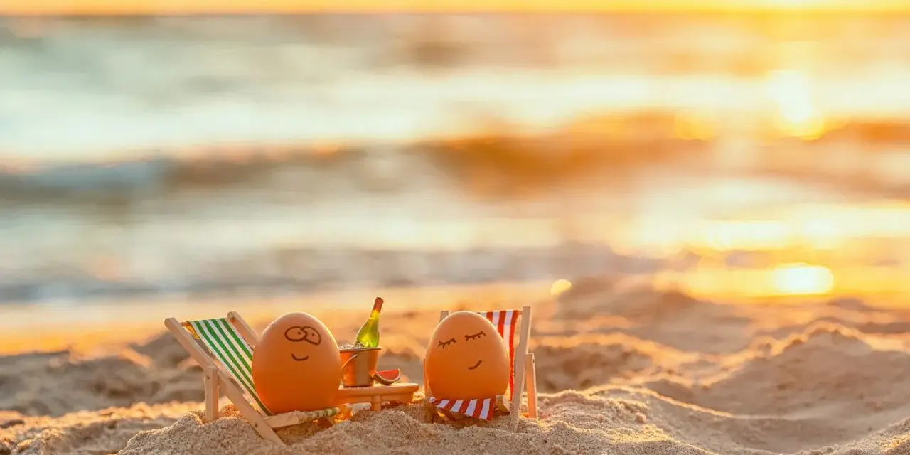 Zwei bemalte Eier entspannen sich in Liegestühlen am Strand bei Sonnenuntergang. Eine Flasche Sekt steht bereit. Eine süße Idee für Veranstaltungen an Ostern.