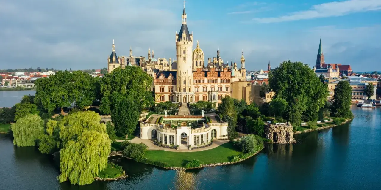 Schweriner Schloss auf einer Insel, umgeben von Wasser und grünen Bäumen. Ein Märchenschloss, das zu den Schwerin Geheimtipps zählt.