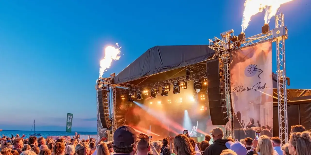 Feuerfontänen lodern bei Konzerten an der Ostsee. Eine Menschenmenge feiert am Strand zu elektronischer Musik.