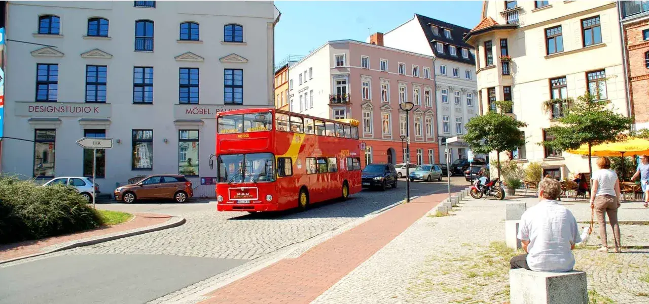Roter Doppeldeckerbus für eine Stadtrundfahrt in Rostock fährt durch eine Gasse mit historischen Gebäuden.