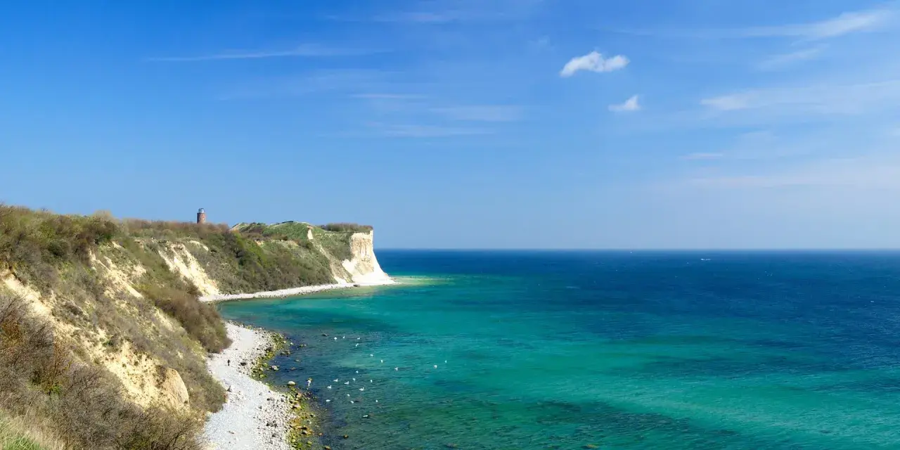 Türkisblaues Meer und Kreidefelsen am Kap Arkona. Ein Leuchtturm wacht über die Küste.