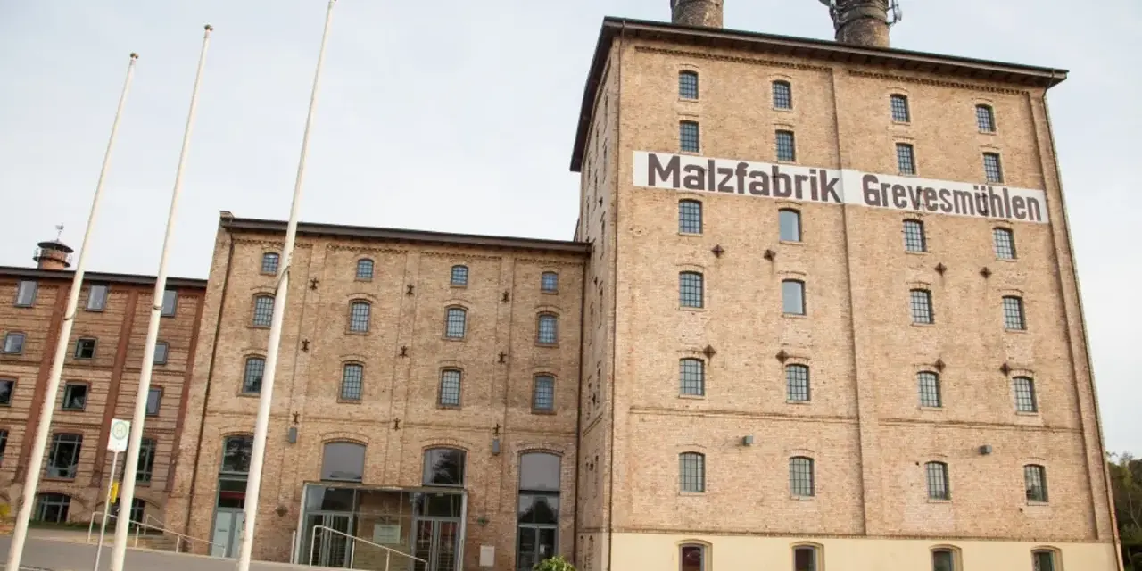 Die imposante Malzfabrik Grevesmühlen, ein Backsteingebäude mit markanten Türmen, steht im hellen Tageslicht.