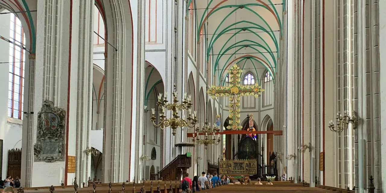Imposanter Innenraum des Schweriner Doms mit Holzbänken, einem großen goldenen Kreuz und grünen Gewölben.