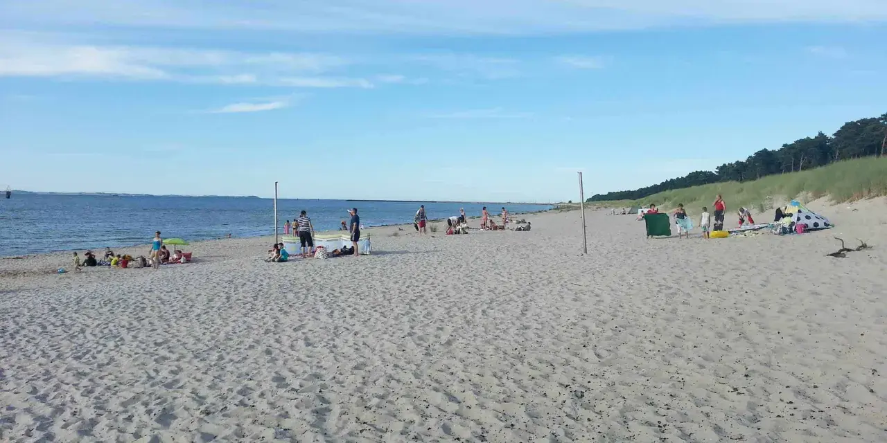 Menschen entspannen sich am sonnigen Lubmin Strand. Das Meer glitzert, der Himmel ist blau mit leichten Wolken.