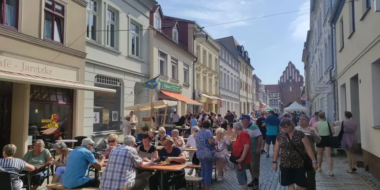 Menschen genießen ein Fest vor dem Kulturhaus Teterow. Viele sitzen an Tischen, essen und unterhalten sich.