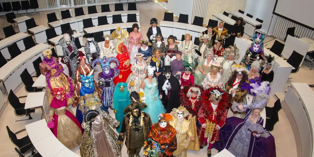 Eine Gruppe in prächtigen Kostümen und Masken, die an venezianische Tage in Schwerin erinnert, versammelt sich in einem modernen Sitzungssaal.