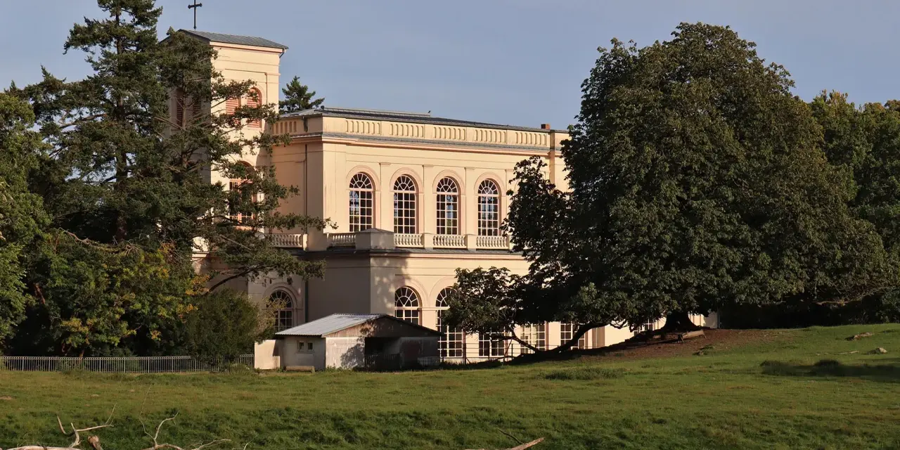 Prachtvolles Gebäude in der **Putbus Altstadt** mit Kirchturm und großen Rundbogenfenstern, umgeben von Bäumen und einer grünen Wiese.
