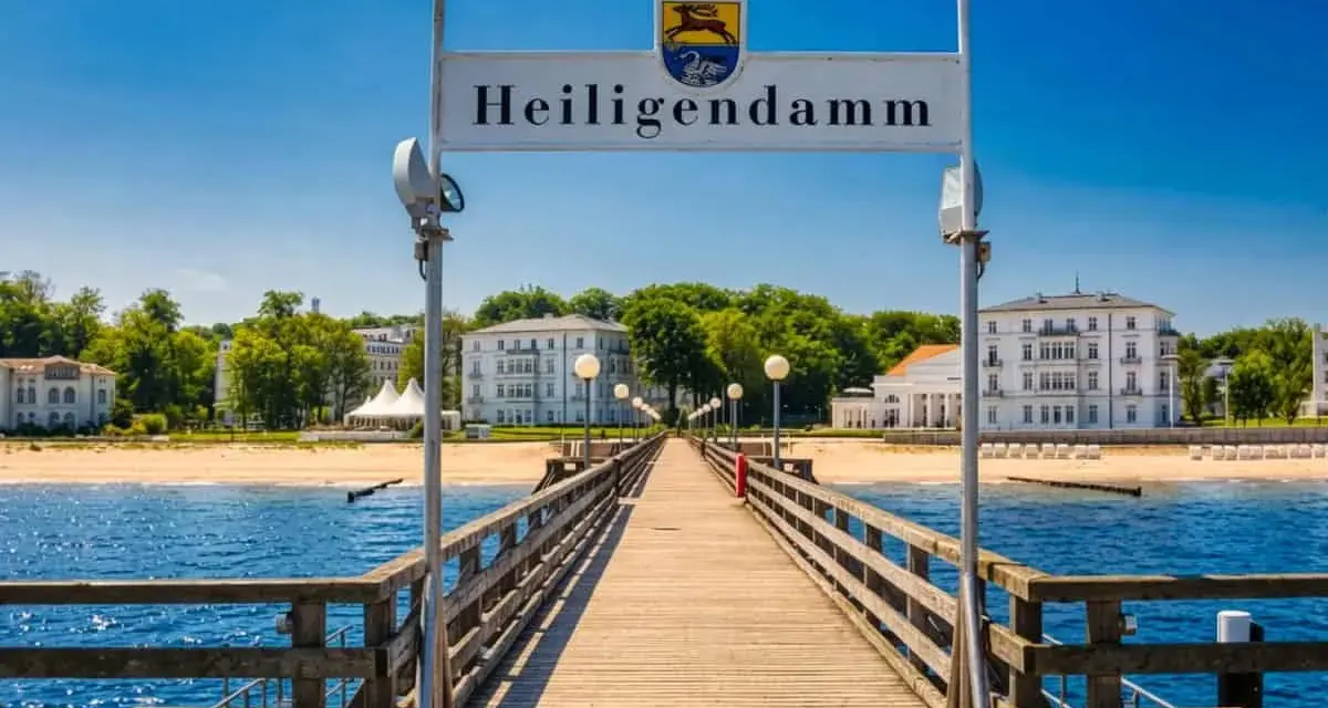 Holzsteg führt zum Heiligendamm Strand mit weißen Gebäuden und blauem Himmel.