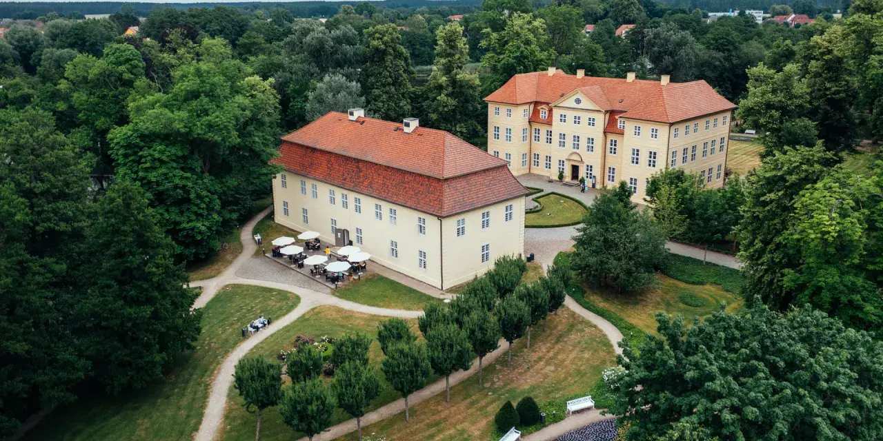 Zwei gelbe Barockschlösser mit roten Dächern auf der Schlossinsel Mirow, umgeben von üppigem Grün und gepflegten Wegen.