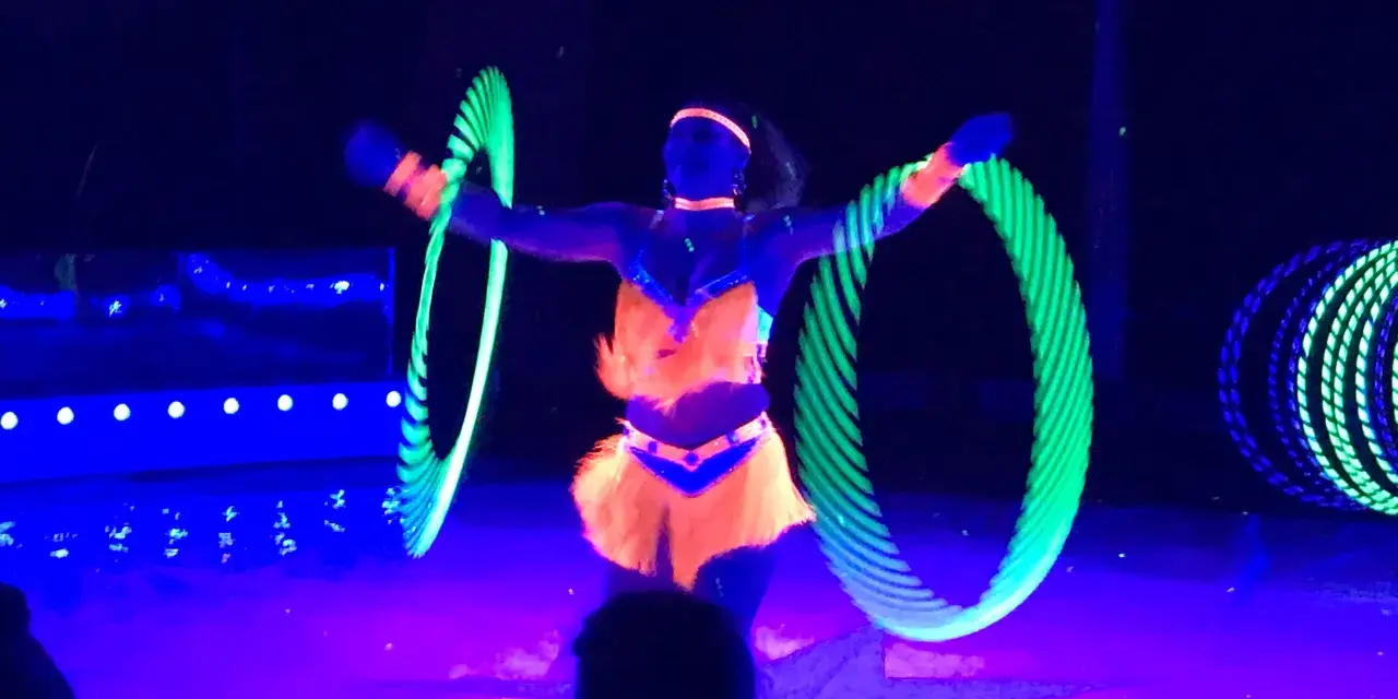 Artistin dreht leuchtende Reifen auf der Bühne des Circus Moreno. Neonfarben und Schwarzlicht erzeugen eine magische Atmosphäre.