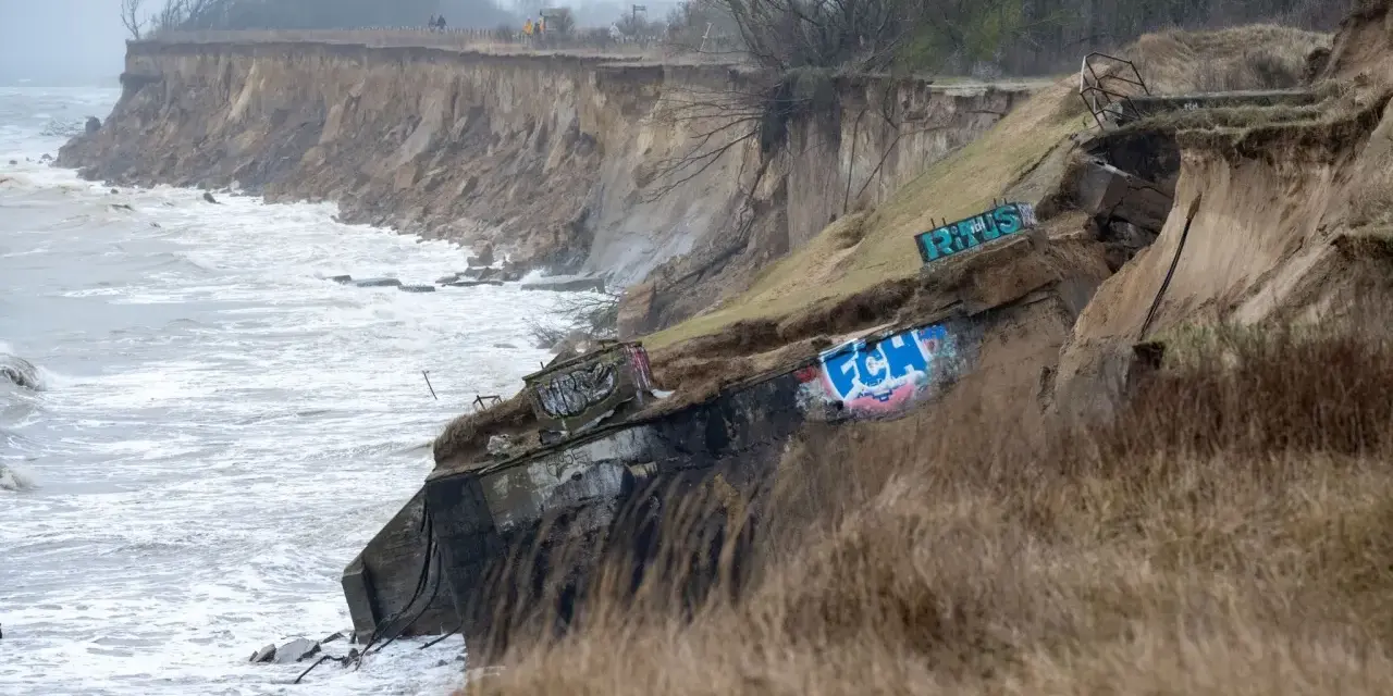 Ein alter Bunker am Strand, von der Erosion freigelegt und mit Graffiti bemalt, trotzt den Wellen.