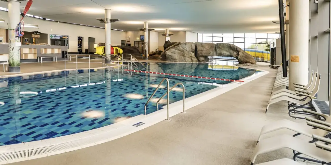 Ein großes Schwimmbecken mit blauen Kacheln und einer Felswand lädt zum Badespaß ein. Hier ist das perfekte Erlebnisbad Ostsee für die ganze Familie.