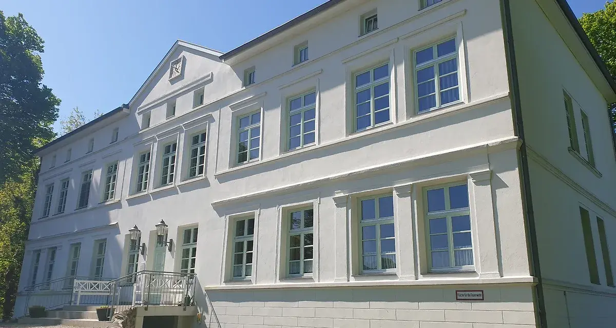 Das Herrenhaus Blengow, ein weißes Gebäude mit vielen Fenstern, steht unter blauem Himmel.