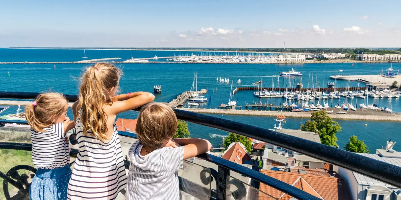 Drei Kinder blicken auf einen belebten Hafen mit vielen Segelbooten. Ein schöner Tag für Veranstaltungen MV mit Kindern.