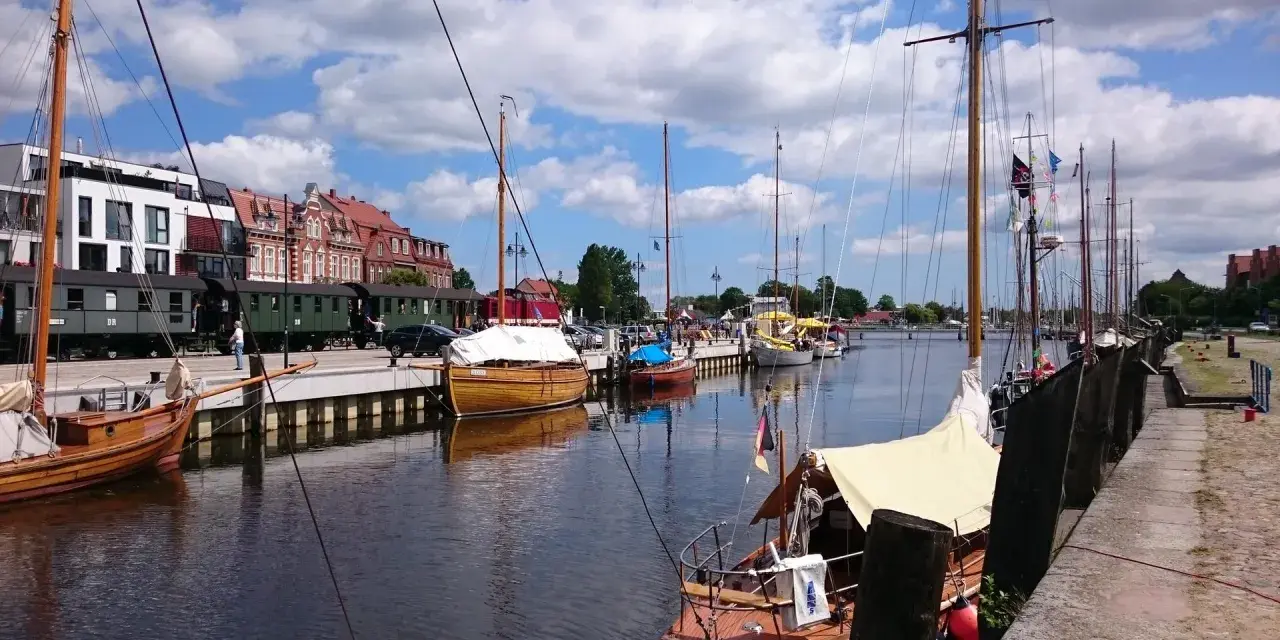 Boote im Greifswald Hafen liegen neben historischen Zügen.