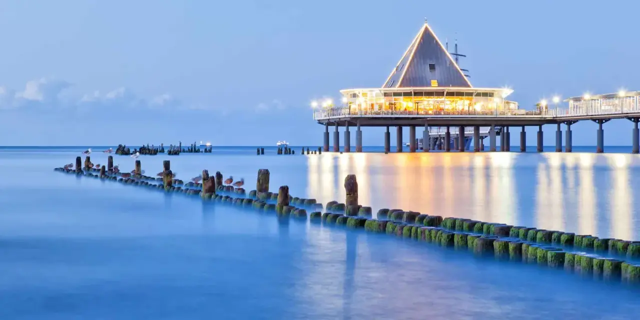 Ein beleuchteter Pier mit Restaurant und Wellenbrechern im Meer. Perfekt für einen Heringsdorf Urlaub.