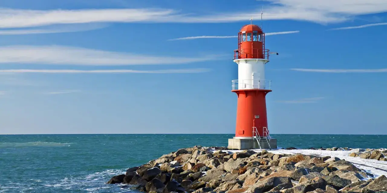 Roter Leuchtturm auf felsiger Mole am barth strand. Blaues Meer und Himmel mit Wolken.
