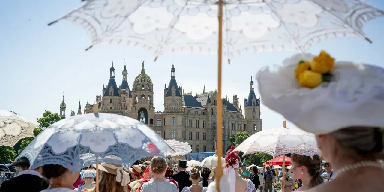 Besucher im historischen Gewand mit Sonnenschirmen beim Altstadtfest Schwerin vor dem Schloss.