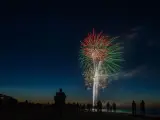 Silhouetten von Menschen am Strand beobachten ein beeindruckendes Feuerwerk über dem Meer. Ein leuchtendes Spektakel in Rot und Grün erhellt den Nachthimmel. Feuerwerk Usedom.
