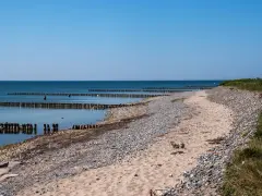Ein ruhiger Tag am Dranske Strand. Holzpfähle ragen aus dem ruhigen Meer, das sich unter einem klaren blauen Himmel erstreckt.