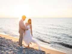 Ein glückliches Brautpaar feiert seine Hochzeit am Strand. Die Sonne geht unter und taucht die Szene in warmes Licht.