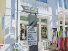 Schild an der Kunstmeile Binz: Keramik, Schmuck, Porzellan, Glas, Textil, Malerei, Fotografie, Bar & Café. Bunte Schals hängen davor.