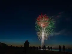 Silhouetten von Menschen am Strand beobachten ein beeindruckendes Feuerwerk über dem Meer. Ein leuchtendes Spektakel in Rot und Grün erhellt den Nachthimmel. Feuerwerk Usedom.