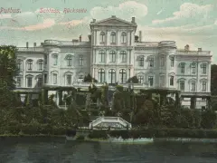 Das Schloss Putbus, von der Rückseite betrachtet, thront majestätisch über einem üppigen Garten und einem ruhigen Gewässer.