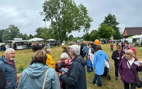Menschen genießen das inselfest Mirow bei bewölktem Himmel. Stände und Bäume säumen die grüne Wiese.