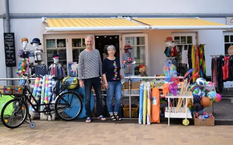 Ein Paar vor einem Laden mit Strandartikeln. Sie sind bereit, juliusruh einkaufen zu gehen und haben alles für einen schönen Tag am Meer.