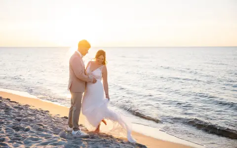 Ein glückliches Brautpaar feiert seine Hochzeit am Strand. Die Sonne geht unter und taucht die Szene in warmes Licht.