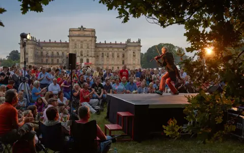 Ein Geiger spielt auf einer Bühne vor einem Schloss, während ein Publikum zusieht. Ein schönes Beispiel für Veranstaltungen an der Ostsee.