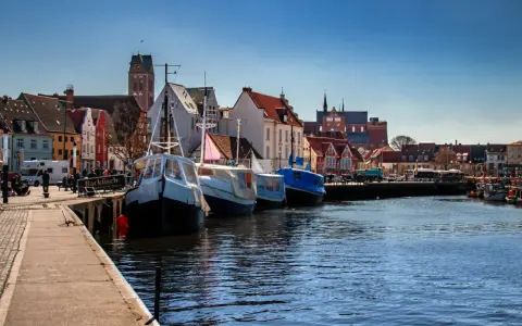 Boote liegen im **Wismar Hafen** vor bunten Häusern. Ein Schild wirbt für "Backfisch".