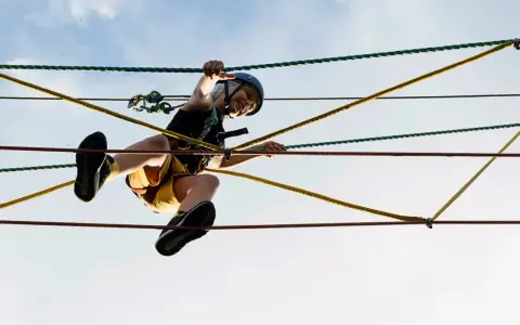 Ein Kind balanciert im Kletterwald Born über Seile. Mit Helm und Sicherung meistert es den Parcours.