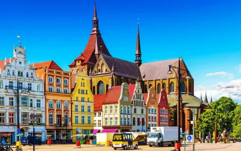 Bunte Giebelhäuser und die Marienkirche prägen das Bild der Rostocker Innenstadt. Ein sonniger Tag auf dem Platz.