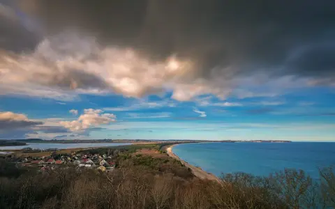 Blick vom Lotsenturm Thiessow über die Küste mit Dorf, Strand und Meer unter dramatischem Himmel.