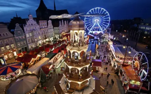Ein beleuchteter Weihnachtsmarkt Mecklenburgische Seenplatte mit Riesenrad, Pyramide und Buden.