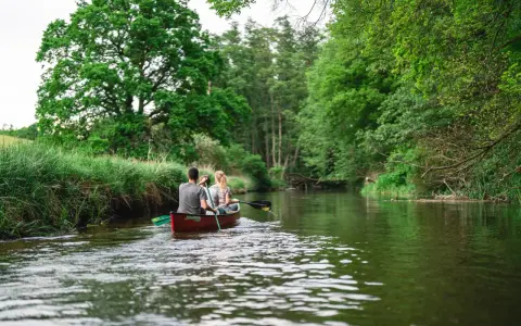 Ein Paar paddelt mit einem Kanu auf einem ruhigen Fluss durch üppige grüne Natur. Ein idyllischer Ausflug in Weitendorf.